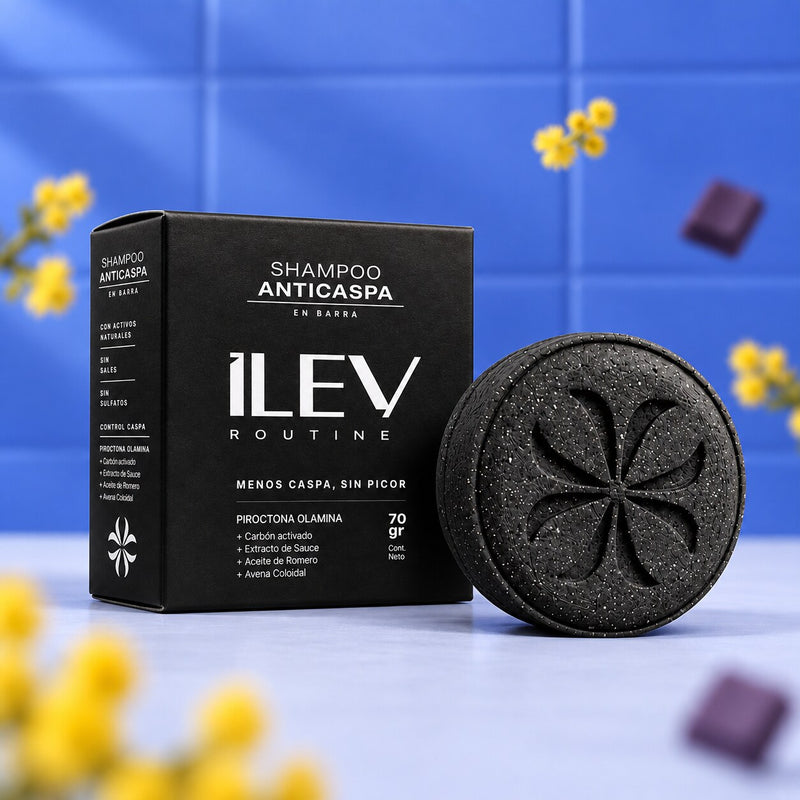 Shampoo Anticaspa en barra ILEV Routine 70 gr, caja negra y barra de carbón activado sobre fondo de baldosas azules con ramas de mimosa amarilla